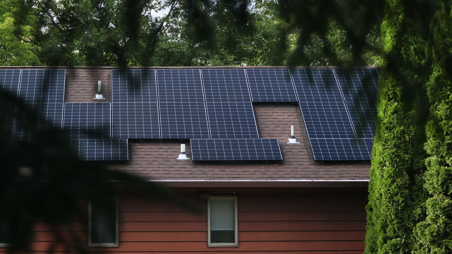 Solar Panels on the roof of a red house framed by a foreground of trees